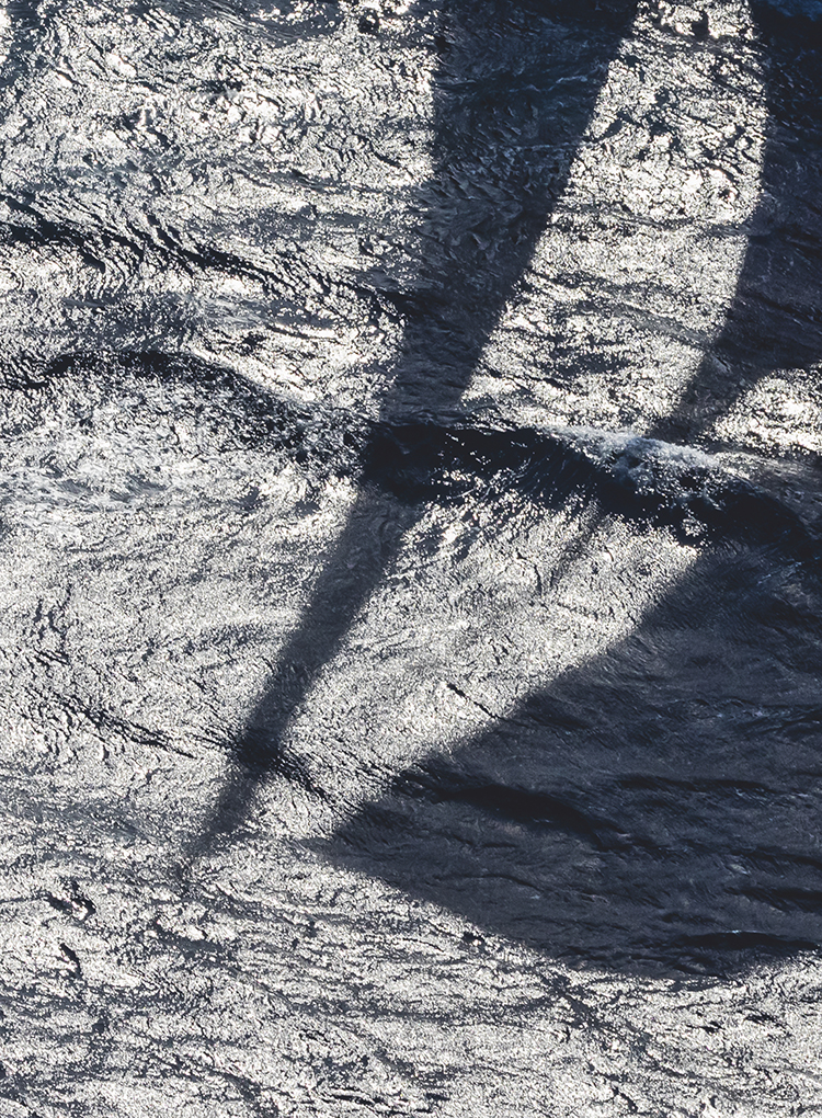 Yacht mast shadow reflecting onto sea