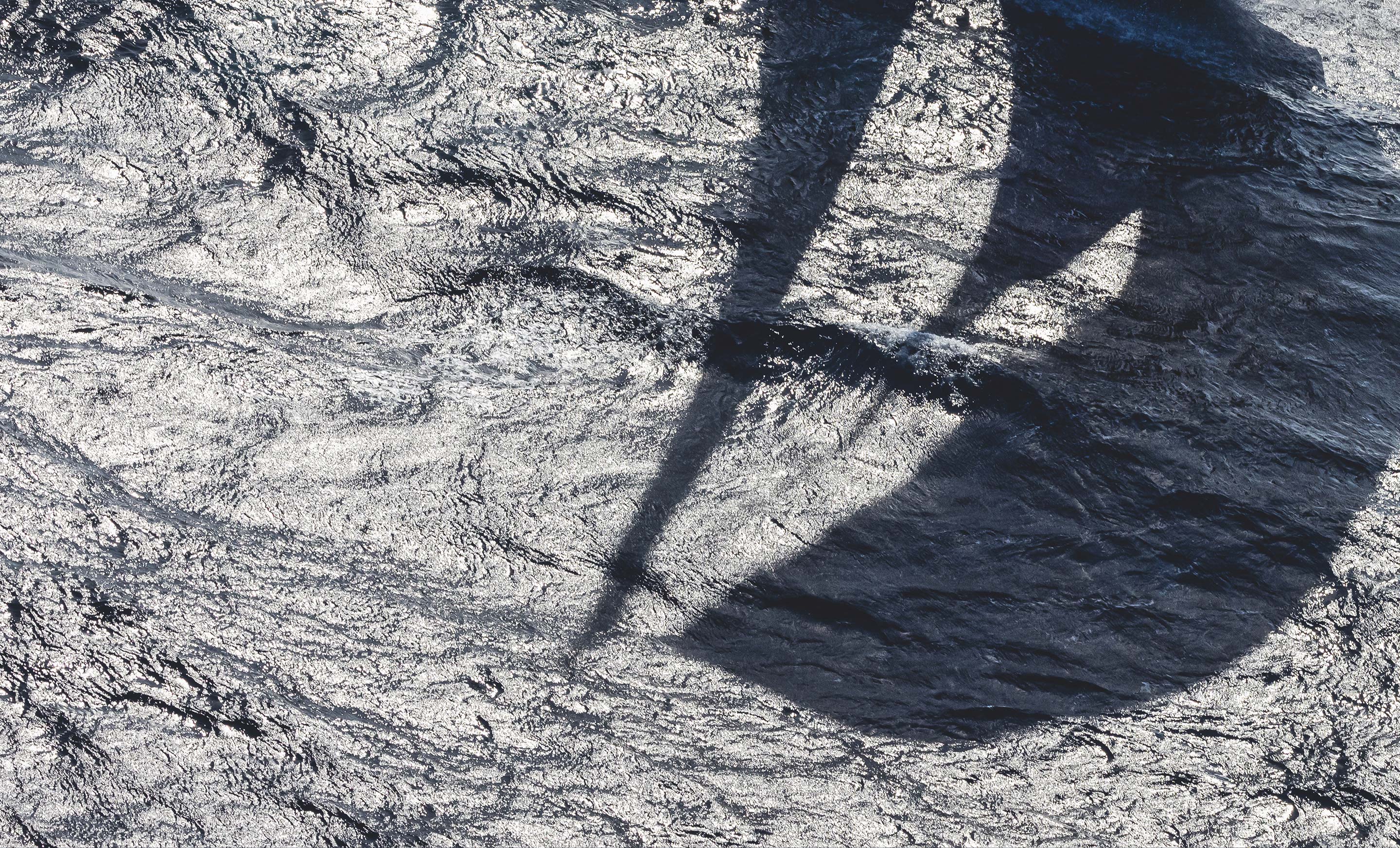 Yacht mast shadow reflecting onto sea